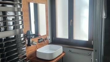 A modern bathroom with a wooden ceiling, a large window, a sink, a bidet, and a towel rack.