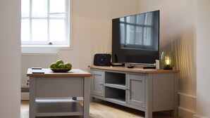 Ein modernes Wohnzimmer mit Flachbildfernseher, Lautsprecher und einem kleinen Tisch mit Äpfeln.