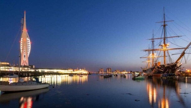 Ein Yachthafen mit einem hohen Gebäude und einem Segelschiff.