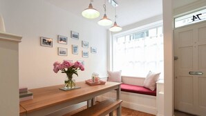 Ein gemütliches Zimmer mit einer hölzernen Bank, einem kleinen Tisch mit Blumenvase und einer Fensterbank mit rotem Kissen.