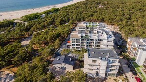 Vista aérea de una zona residencial costera con edificios modernos, una playa y densos pinos.