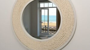 A circular mirror with a woven frame, reflecting a balcony with a view of the beach and the sea.