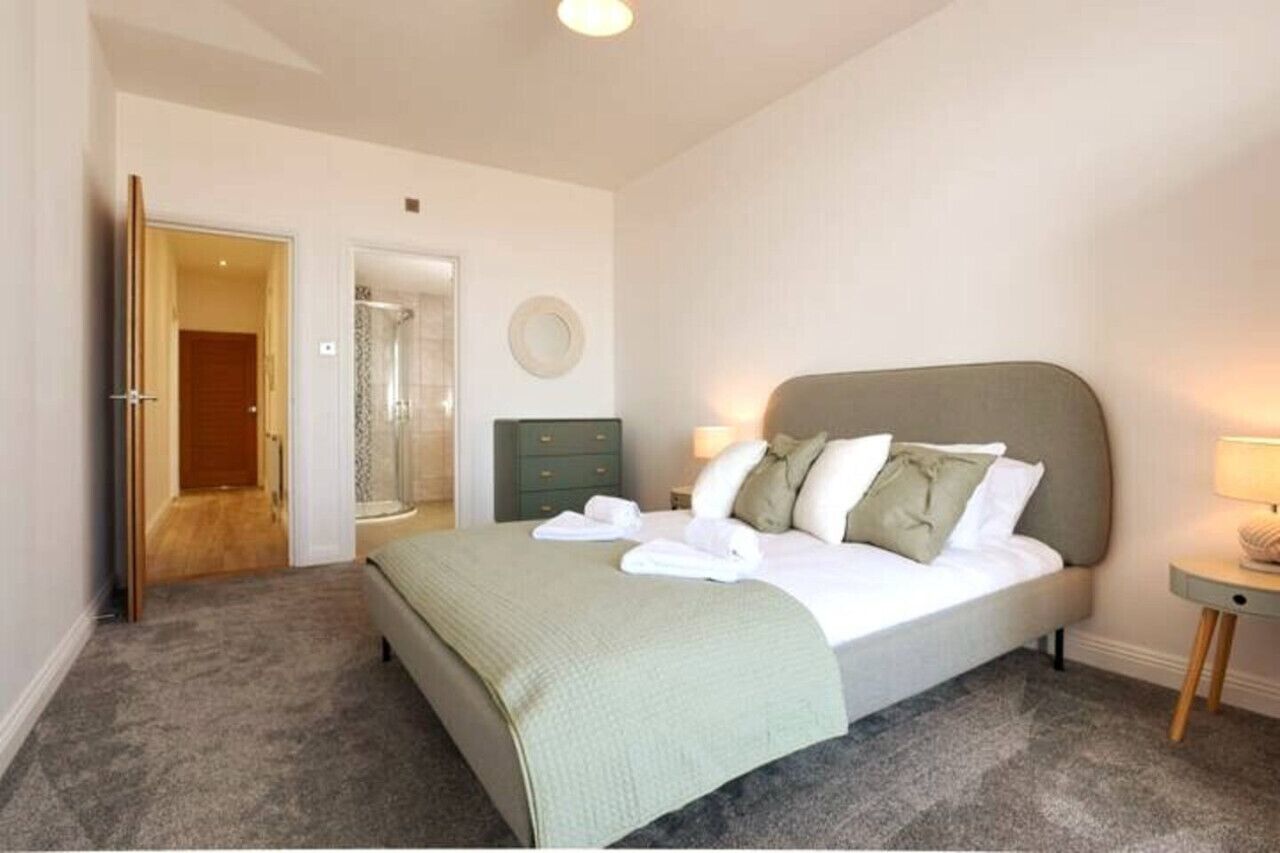 Een slaapkamer met een bed, nachtkastje, spiegel en een deur.