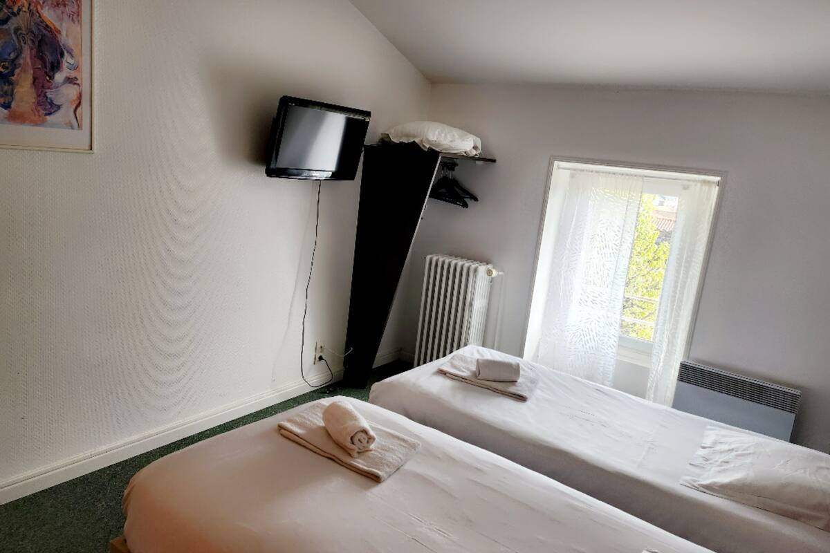 Een hotelkamer met twee bedden, een aan de muur bevestigde televisie en een raam met uitzicht op bomen.