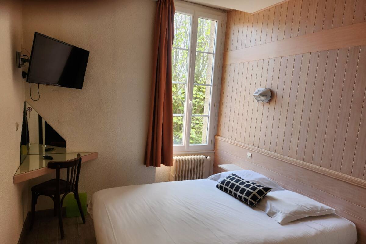 Een slaapkamer met een bed, een bureau, een stoel, een televisie en een raam met gordijnen.