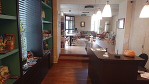 Un área de recepción con un mostrador de madera, una estantería verde con revistas y un comedor con sillas y una mesa.