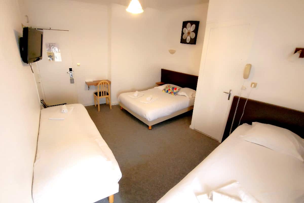 Een hotelkamer met twee enkele bedden, een klein bureau, een stoel, een aan de muur bevestigde televisie en een bloemen schilderij.