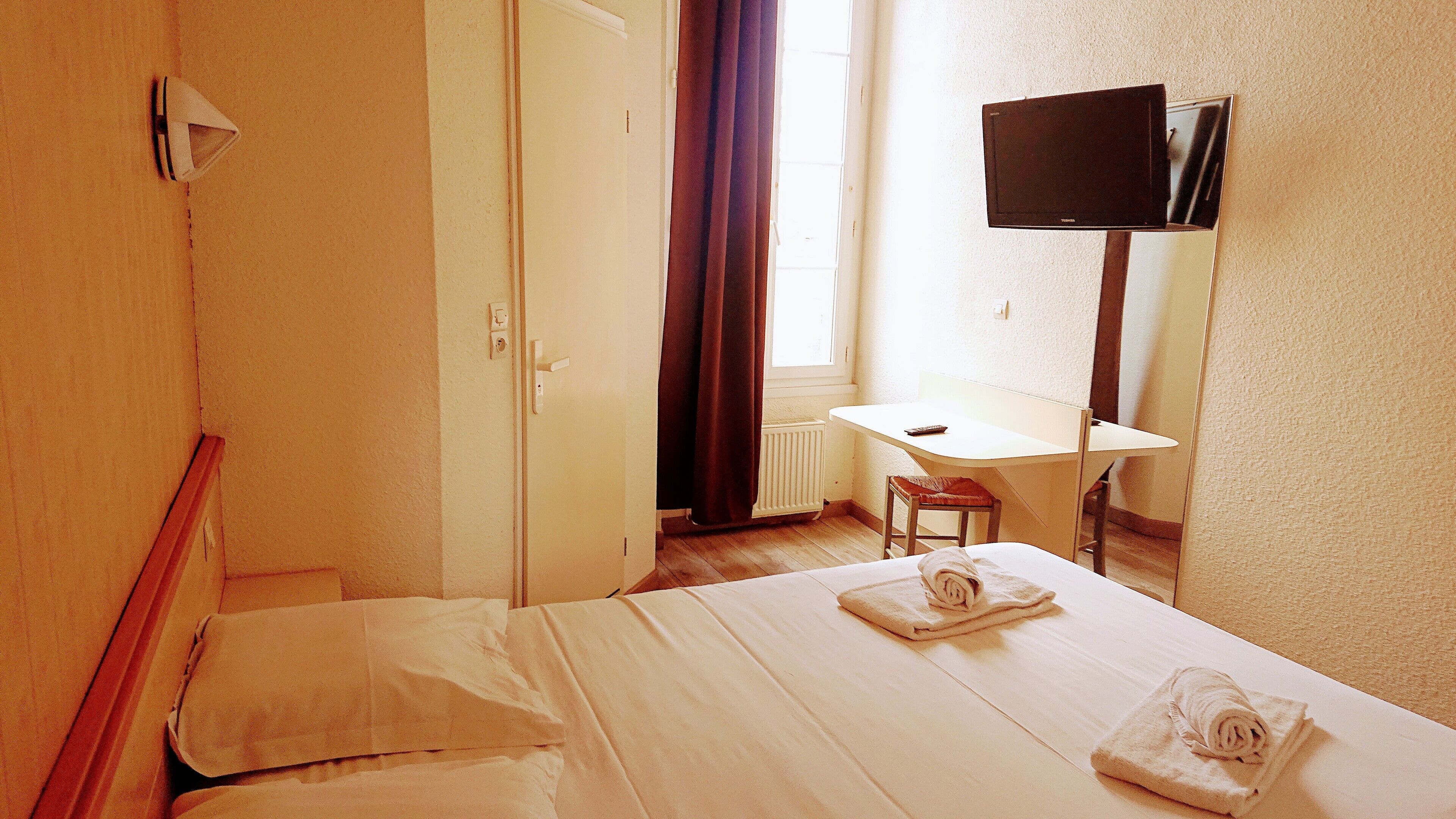 A hotel room with a bed, a desk, a chair, a TV, and a window with curtains.