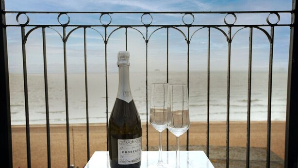 Una botella de Prosecco y dos copas sobre una mesa con vista a la playa.