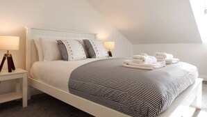 Una cama bien hecha con ropa de cama a rayas, dos lámparas de noche y un par de toallas dobladas sobre la cama.