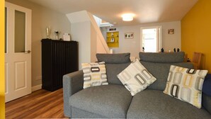 A living room with a grey sofa, patterned cushions, a black cabinet, and a staircase leading to an upper floor. - Parkside Haven | 2BR w/Off-Road Parking (Hampshire)