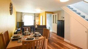 A dining area with a wooden table set for four, a sofa, and a staircase leading to a landing. - Parkside Haven | 2BR w/Off-Road Parking (Hampshire)