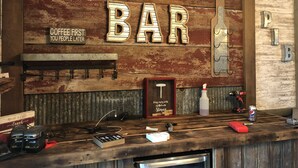 A rustic bar area with wooden walls, a sign that reads "BAR", and various bar tools and supplies on the counter.