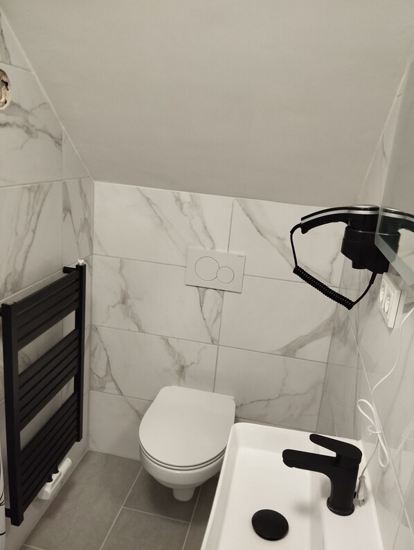 A bathroom with a toilet, a black towel rack, a white sink with a black faucet, and marble-patterned walls.