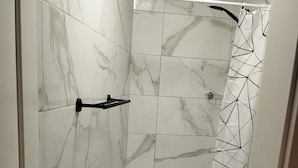Un baño con baldosas de mármol, una cortina de ducha con diseño geométrico y un perchero.