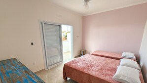 A room with two beds, a wooden table, a ceiling fan, and a sliding door leading to an outdoor area. - São Francisco Flats - Suite dos Sabiás (Guapé)