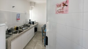 A modern kitchen with a granite countertop, a built-in oven, and a microwave. There is a towel hanging on the wall and a chair near the sink. - São Francisco Flats - Suite dos Sabiás (Guapé)