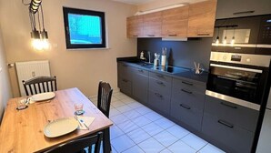 A modern kitchen with grey cabinets, a black countertop, and a built-in oven. There is a dining table with chairs and a window above it. - Zeitwohnung Kenn/region Trier (Kenn)