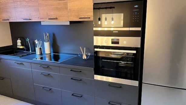 A modern kitchen with a built-in oven and microwave, stainless steel appliances, and a sleek countertop. - Zeitwohnung Kenn/region Trier (Kenn)