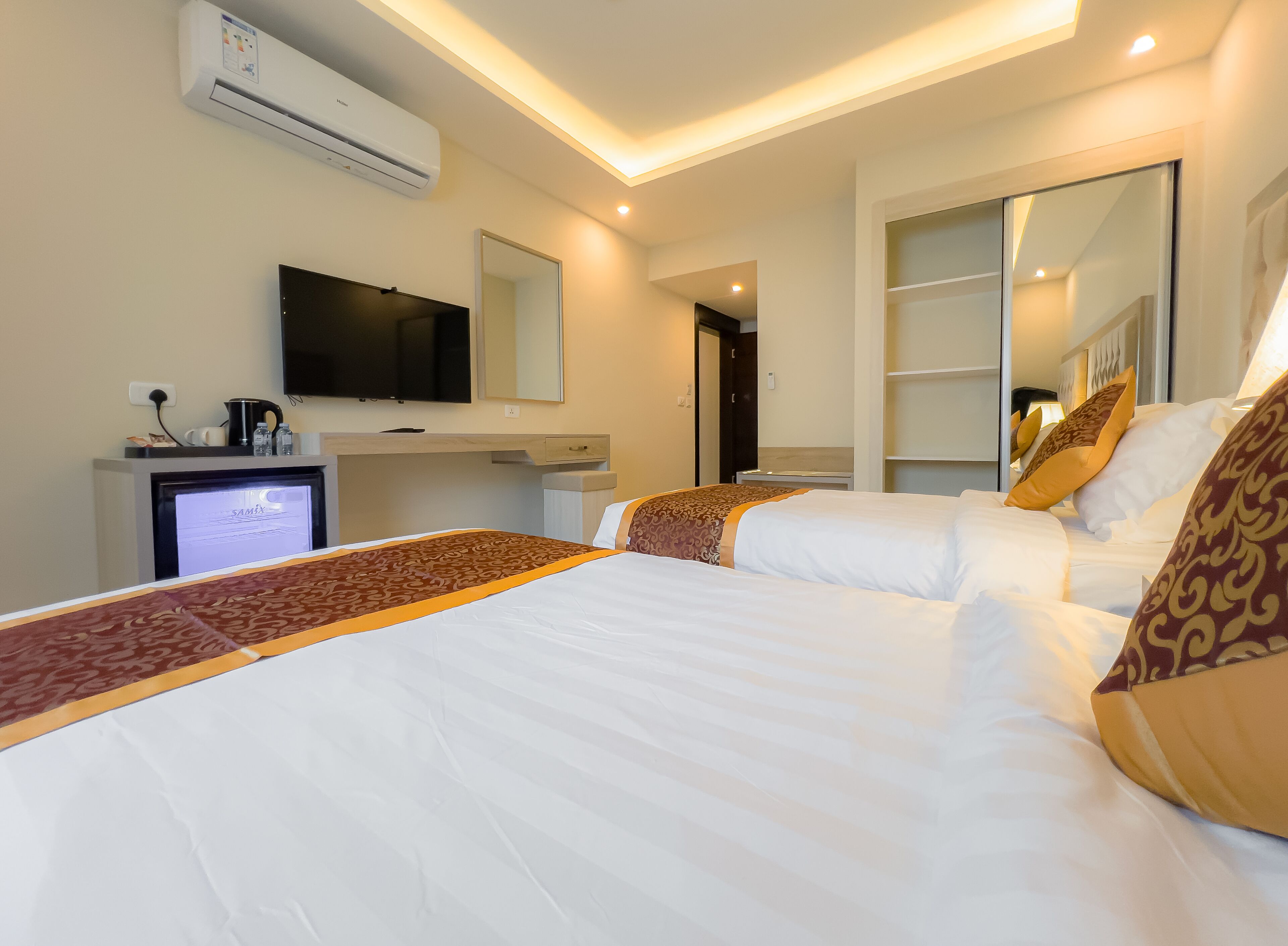 Una habitación de hotel con cama, escritorio, computadora, televisor y espejo.