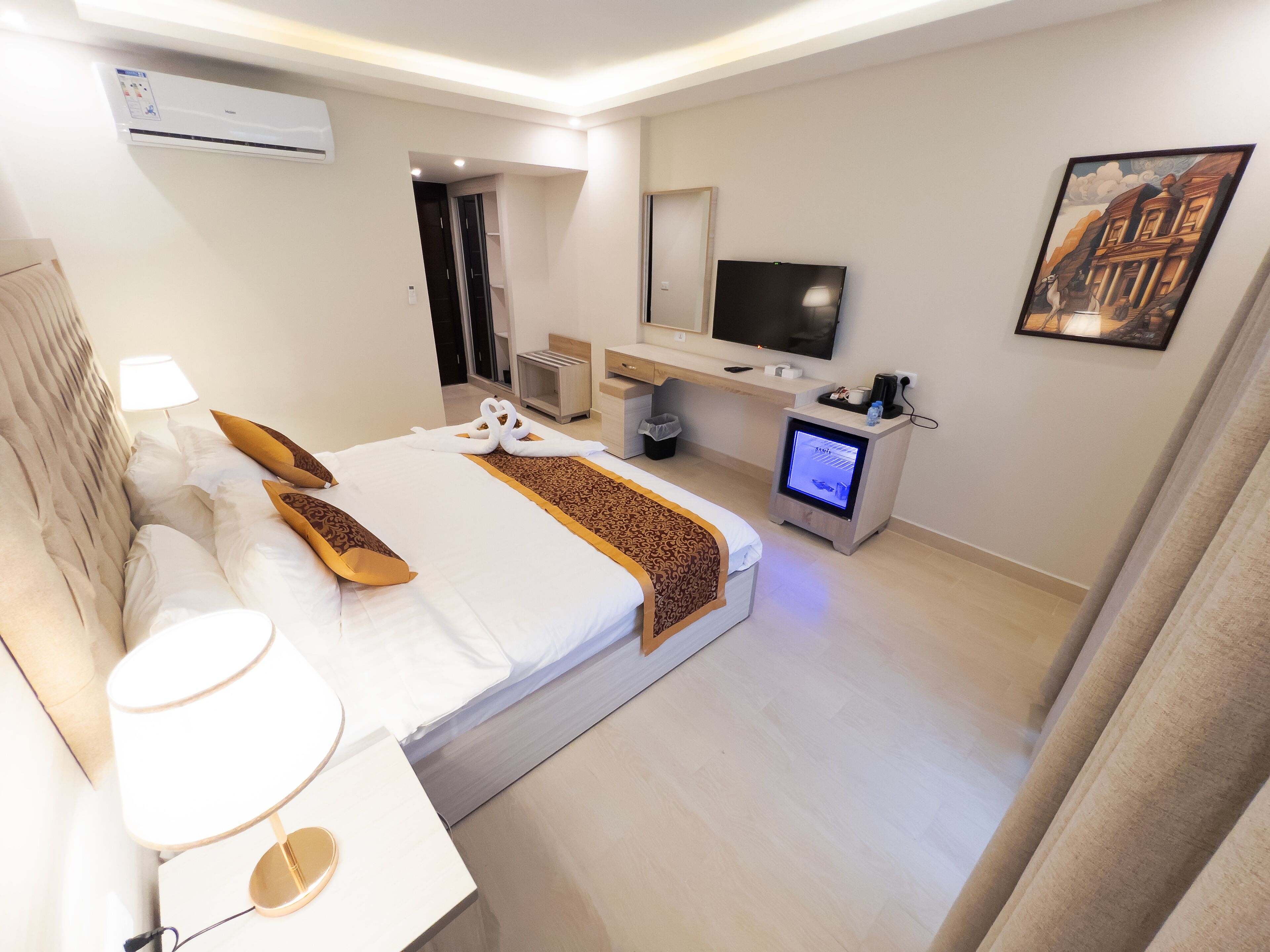 A hotel room with a large bed, a TV, a desk with a computer, and a painting on the wall.