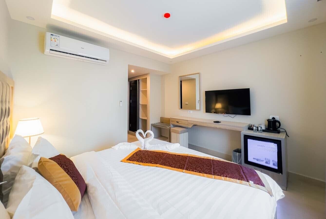 A hotel room with a bed, a TV, an air conditioning unit, a desk, and a coffee machine.