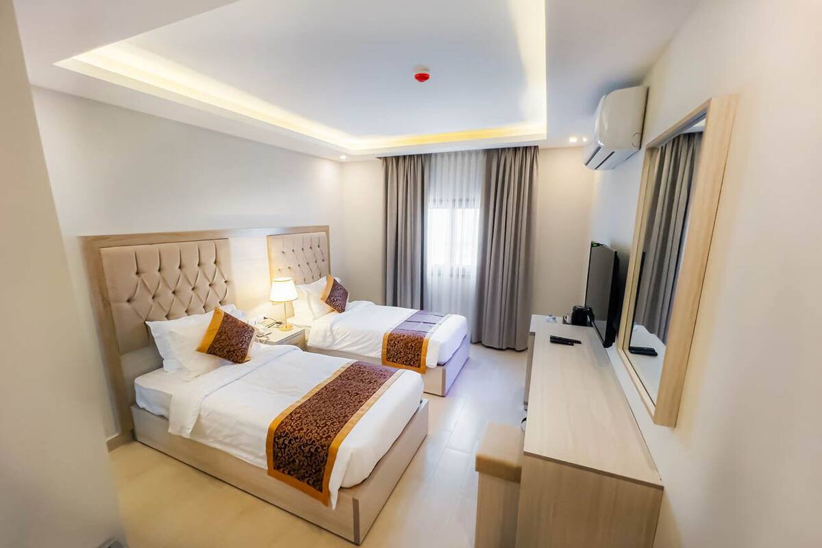 A hotel room with two beds, a desk, a mirror, and a ceiling light.
