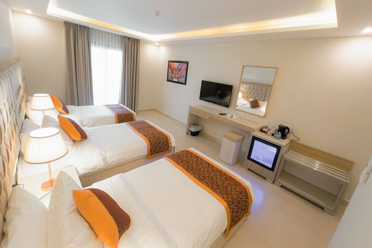 A hotel room with two beds, a desk with a computer, a TV, and a mirror.