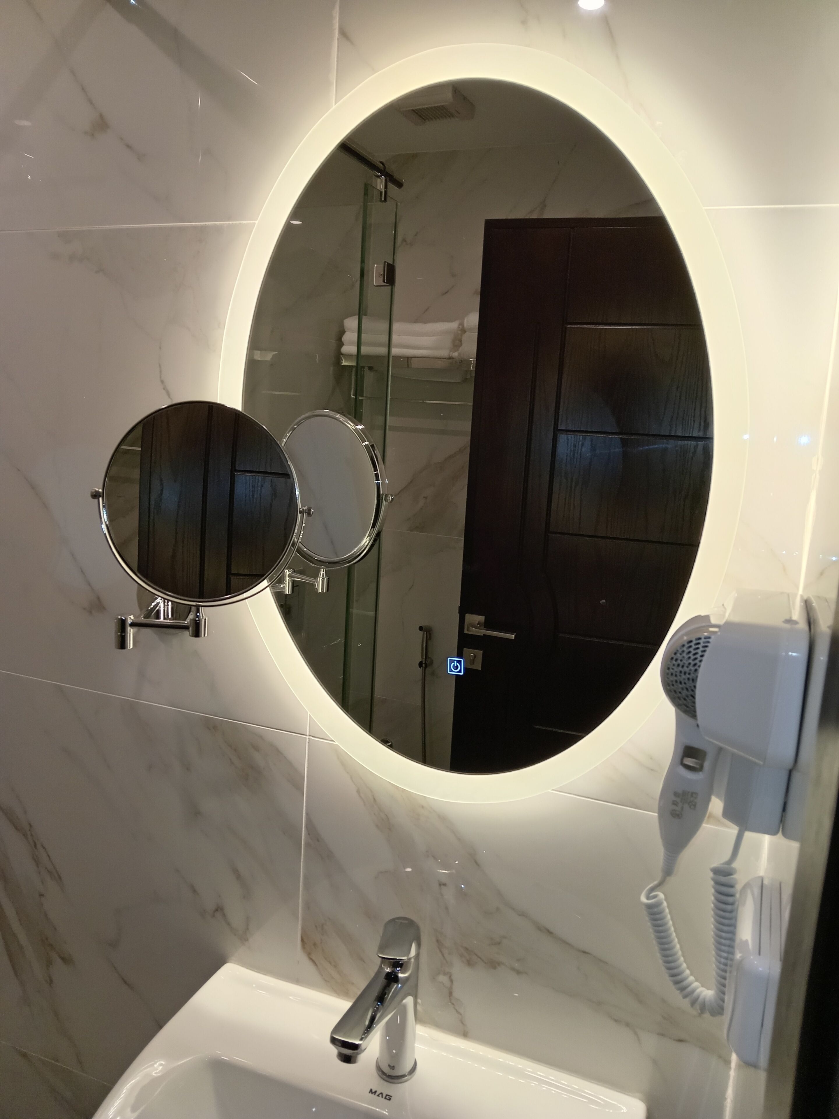 A bathroom with a round mirror, two smaller mirrors, a hairdryer, and a sink with a faucet.