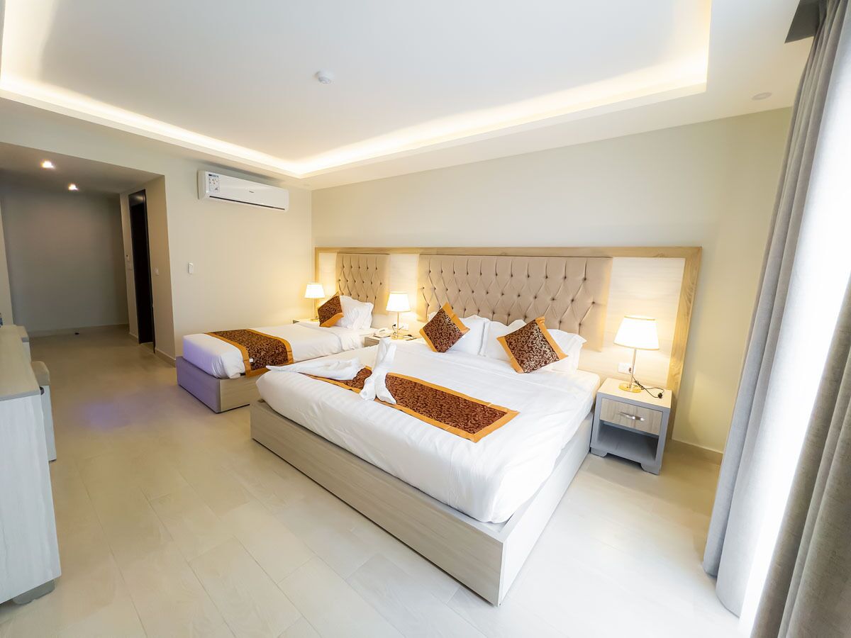 A hotel room with a large bed, bedside tables, a wardrobe, and an air conditioning unit.