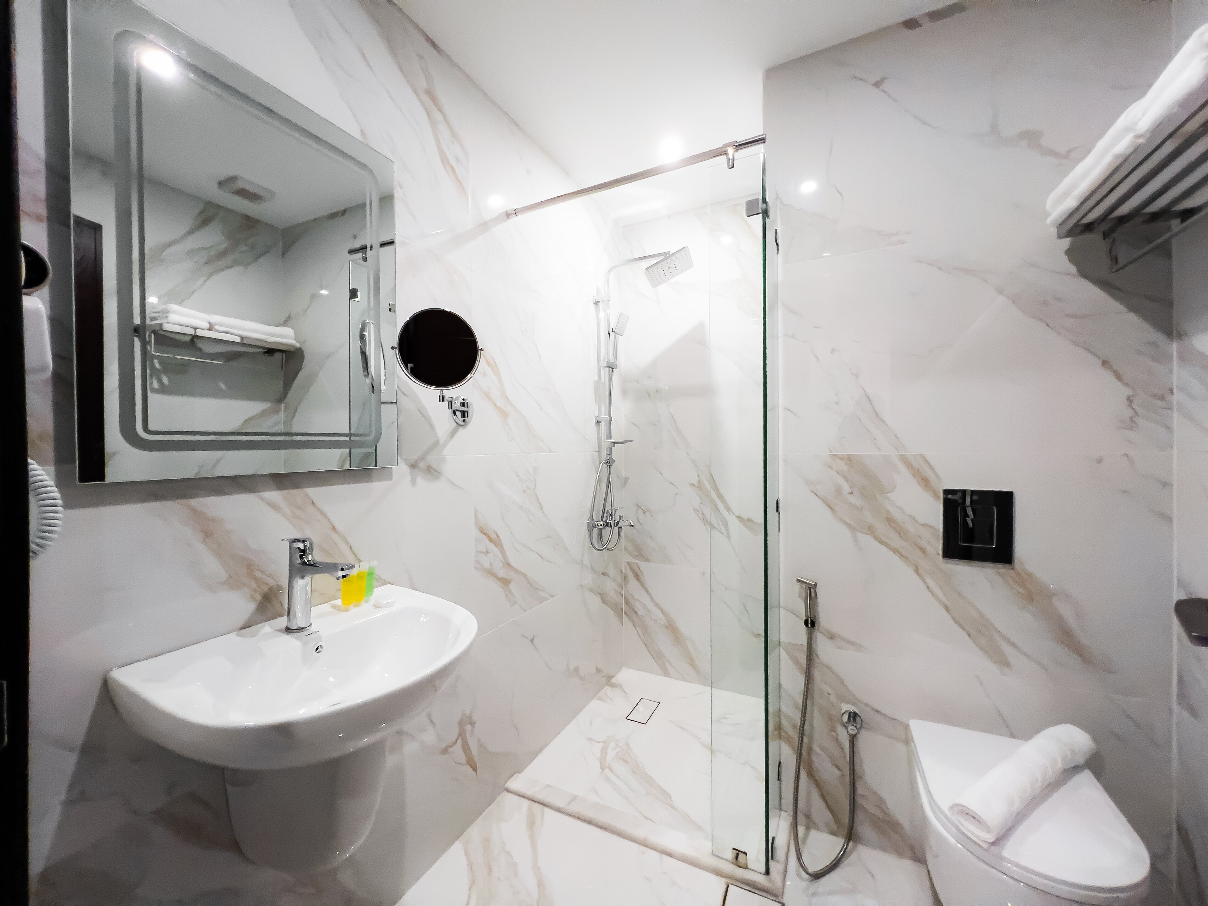 A modern bathroom with a marble floor, a glass shower enclosure, a white sink, and a toilet.