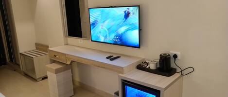 A modern living room with a flat-screen TV mounted on the wall, a wooden desk with a laptop, and a small TV on a stand.