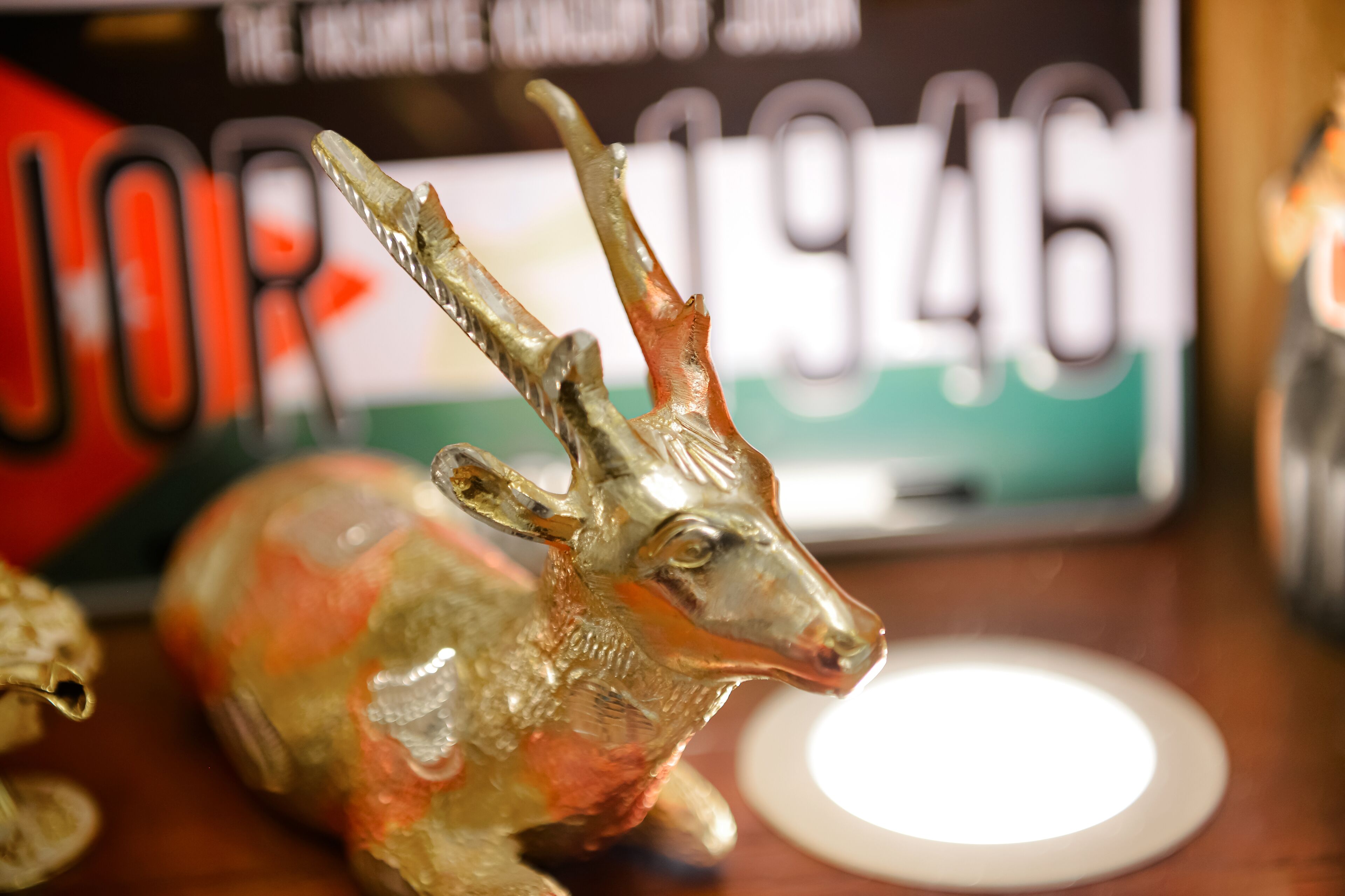 A decorative deer figurine on a table with a blurred background featuring a sign with numbers.