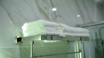 A neatly folded white towel on a metallic towel rack in a bathroom with a marble wall.