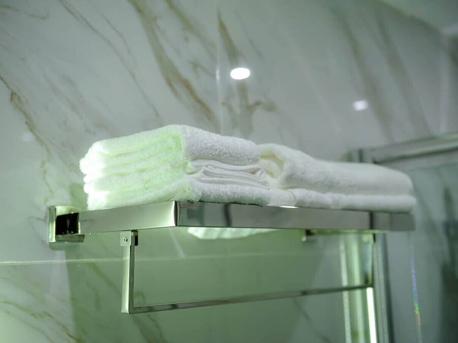 A neatly folded white towel on a metallic towel rack in a bathroom with a marble wall.