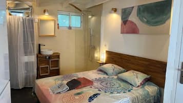 Un dormitorio con cama, mesita de noche, espejo, ducha y ventana.
