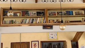 A room with wooden bookshelves filled with books and decorative items, a hanging light bulb, and a framed picture on the wall. - RESIDENCE AINA (Abomey-Calavi)