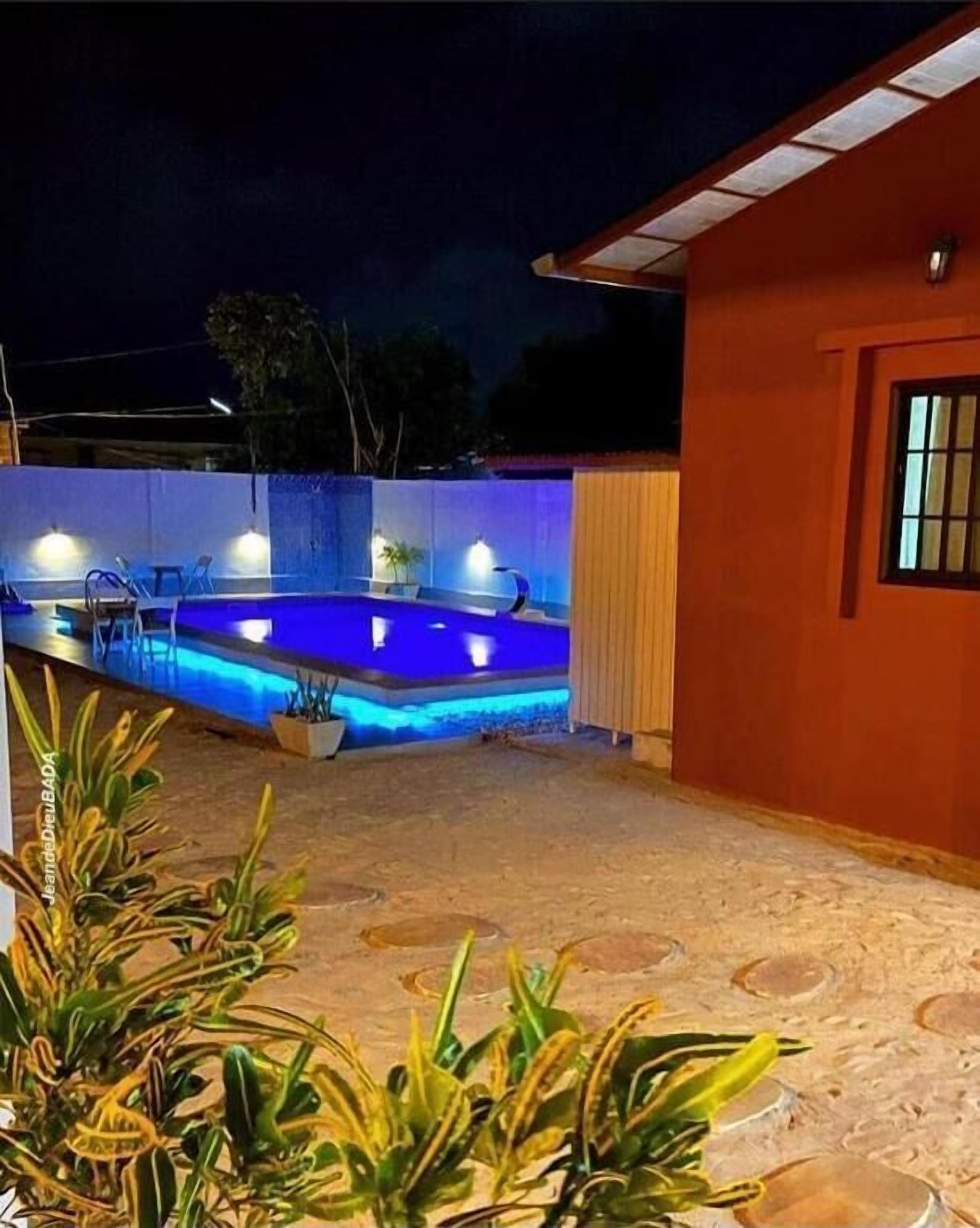A swimming pool with blue lighting, surrounded by a house with a red exterior and a window.