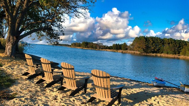 Un entorno junto al lago con cuatro sillas Adirondack y una canoa en la arena.