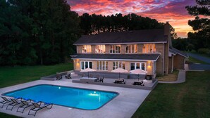 Una casa de dos pisos con piscina, mobiliario exterior y un césped bien cuidado.