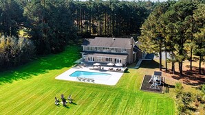 Una casa grande con piscina, rodeada de un césped cuidado y árboles.