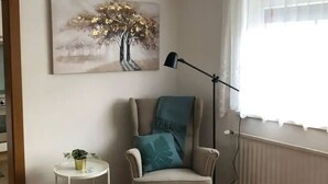 A room with a chair, a small table with a plant, a floor lamp, and a painting on the wall. - Apartment mit Gartenblick (Aldrans)