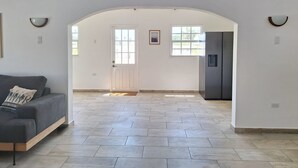 A spacious living room with a grey sofa, a door leading to another room, and a large window. - NEW! Villa La Brisa Aruba│Beautiful&Relaxing: Private pool,8-Min Stroll to Beach (Noord)