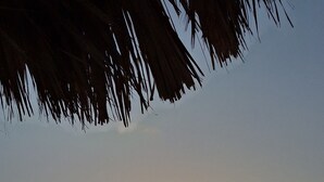 A beach scene with the sun setting over the ocean, a sandy shore, and a thatched roof structure. - NEW! Villa La Brisa Aruba│Beautiful&Relaxing: Private pool,8-Min Stroll to Beach (Noord)