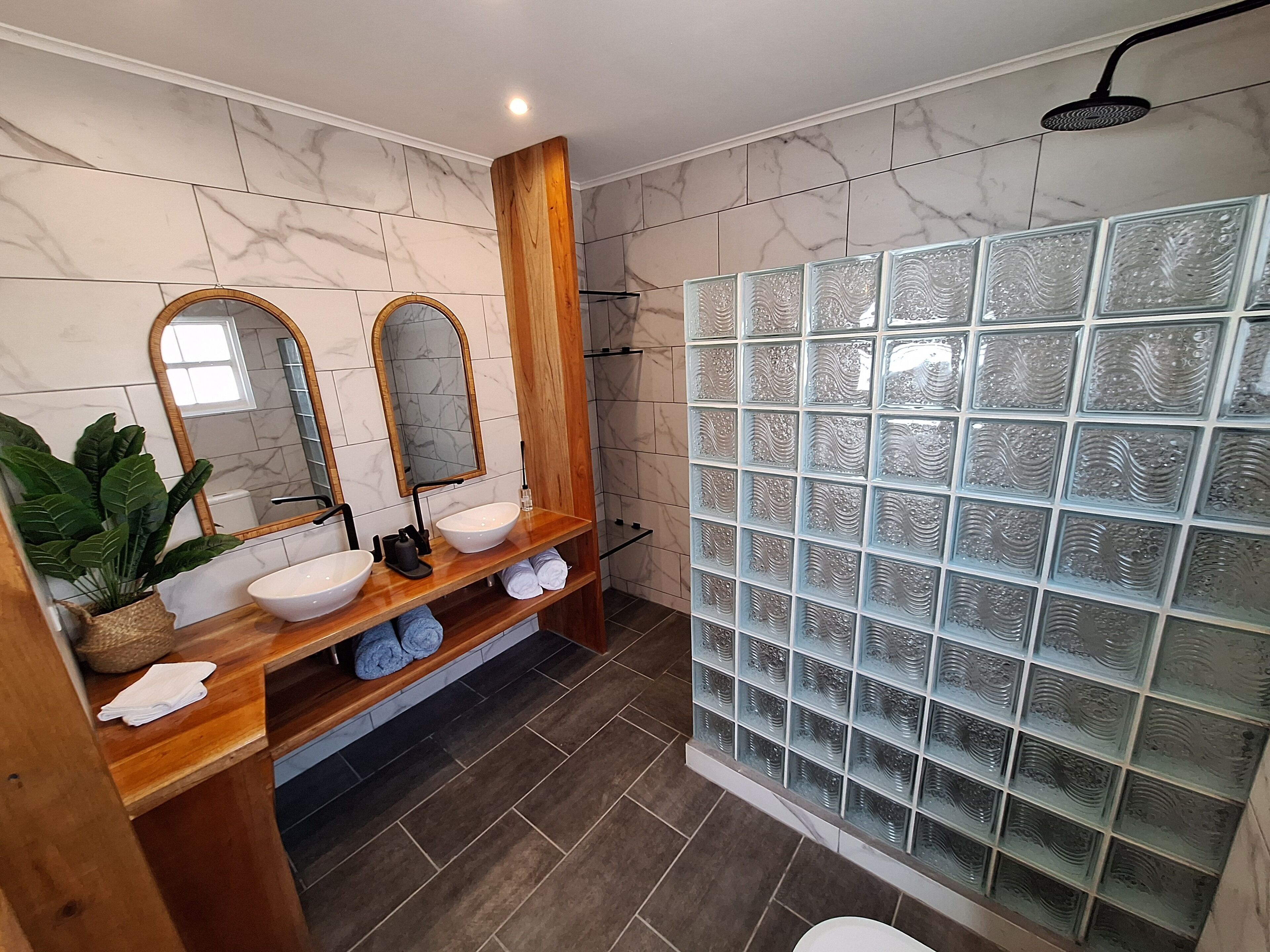 A modern bathroom with a wooden vanity, two sinks, a large mirror, and a glass shower enclosure.