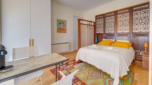 Un dormitorio con cama, escritorio, silla, radiador, alfombra colorida y un separador de madera.