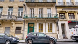 Un edificio de varios pisos con una puerta verde, balcones y un coche estacionado.