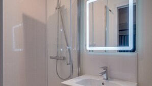 Un baño moderno con ducha de vidrio, lavamanos blanco y espejo con marco iluminado.