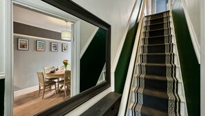Un escalier avec une rampe aux motifs noir et blanc, un coin repas avec une table dressée pour quatre personnes, et des tableaux encadrés accrochés au mur.