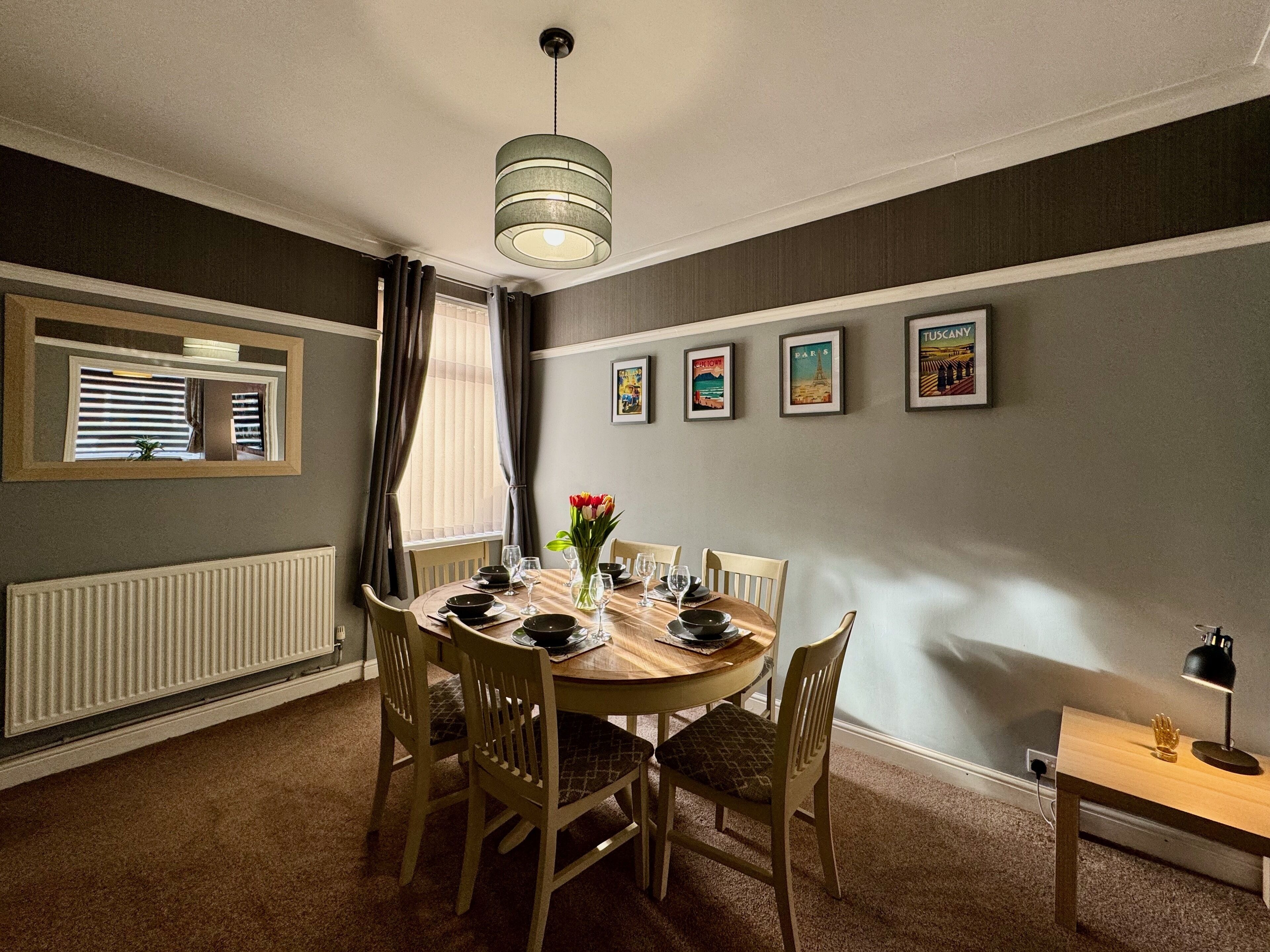 Een eetkamer met een ronde tafel, zes stoelen, een bloevas en een hanglamp.